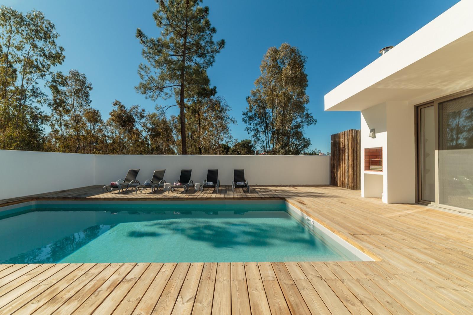 Piscina con deck de madera y tumbonas en una vivienda de una planta